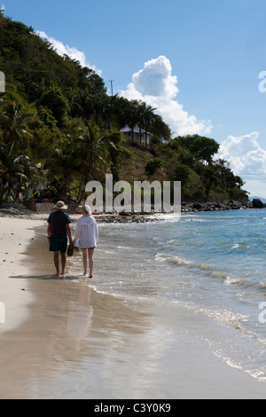 Scène romantique de l'homme et de la femme marchant le long de plage avec des palmiers le long du littoral vallonné à Tortola, Îles Vierges Britanniques Banque D'Images
