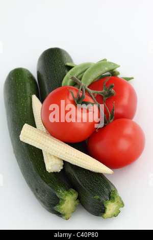 Gros plan d'une sélection de légumes frais crus sains tomates rouges, courgettes, petits pois et de maïs sur un fond blanc. Banque D'Images