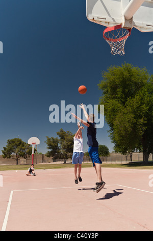 Garçons jouant au basket-ball à un parc de quartier en plein air un garçon regarde sur l'attente à son tour de jouer Banque D'Images