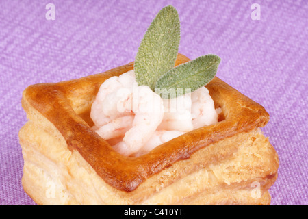 Close-up d'un vol-au-vent aux petites crevettes cuites décorées avec sage. Sur un fond de tissu rose Banque D'Images