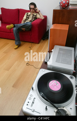 Homme assis sur un canapé rouge en écoutant de la musique sur le casque d'un microsillon player Banque D'Images