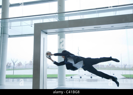 Businessman catching soccer ball in lobby Banque D'Images