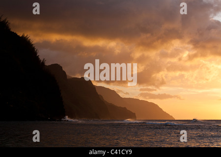 Nā Pali Coast vagues au coucher du soleil. Coup vagues dans le vent que les nuages sont éclairés par le soleil couchant. Banque D'Images