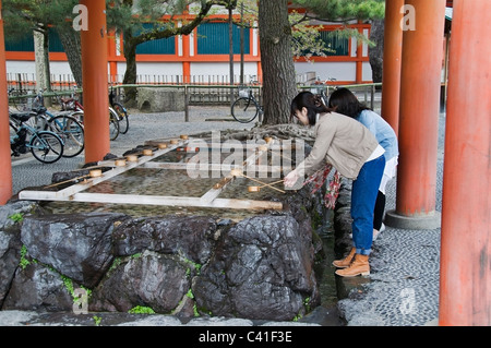 Deux jeunes femmes, une pratique Temizu rituel de purification de cérémonie à un lavage à la main et la purification fontaine à Heian-Jingu Shrine Banque D'Images