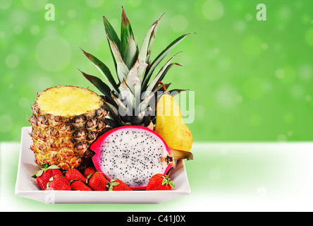 Bienvenue dans les tropiques : fruits tropicaux frais servi dans une assiette blanche sur fond vert fun. Banque D'Images