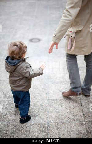 Père d'atteindre pour la main de bébé sur trottoir, cropped Banque D'Images