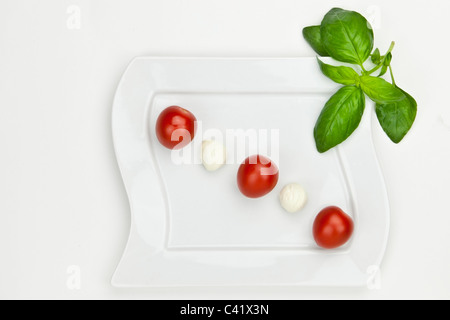 Boules de mozzarella avec tomates cerises sur une plaque blanche Banque D'Images
