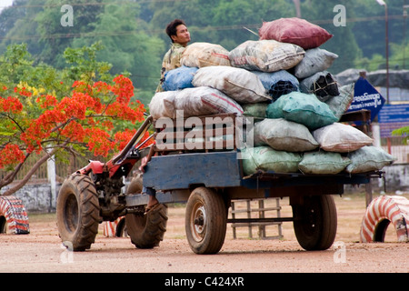 Un homme sur un tracteur est la prestation de gros sacs de charbon de bois Les poêles à bois dans le Laos communiste. Banque D'Images