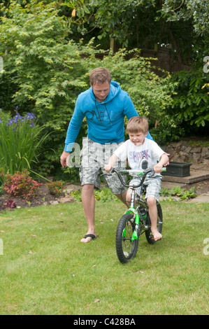 Père dans le jardin arrière d'enseigner son fils faire du vélo Banque D'Images
