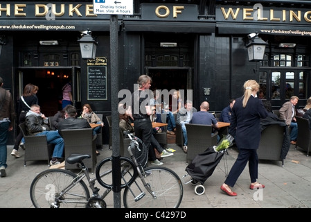 Foule assis outstide le duc de Wellington pub sur Portobello Road le samedi matin, Notting Hill Gate, London England UK Banque D'Images