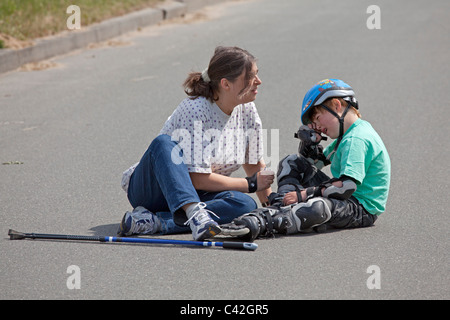 Une femme d'âge moyen réconfortant son jeune fils qui s'est fait mal à le patin à roulettes Banque D'Images