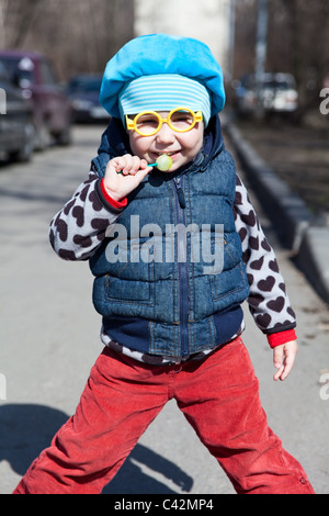 Petit enfant russe avec lollipop est debout à l'extérieur. Lunettes drôles comme Harry Potter Banque D'Images