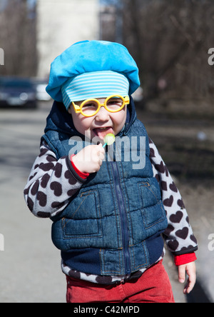 Petit enfant russe avec lollipop est debout à l'extérieur. Lunettes drôles comme Harry Potter Banque D'Images