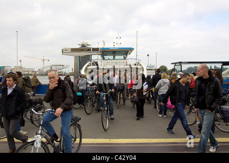 Les cyclistes quitter le ferry qu'ils sont montés à bord pour traverser la rivière/canal dans une hâte à Amsterdam Banque D'Images