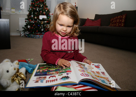 Le jour de Noël petite fille (presque 3) regarde à travers un livre qu'elle a été donné, avec ses personnages favoris Banque D'Images