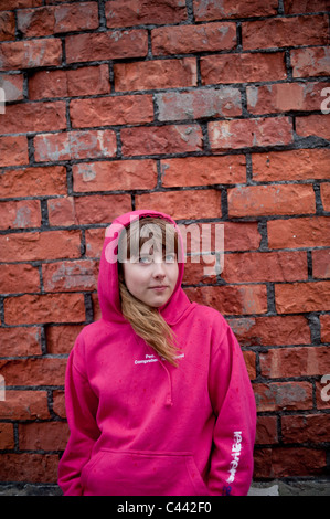 Une jeune fille portant un haut à Capuchon Sweat rose en face d'un mur de briques, UK Banque D'Images
