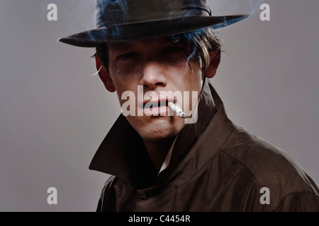Portrait d'un homme portant un chapeau et trench coat en fumant Banque D'Images
