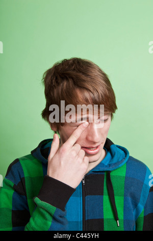 Un adolescent se frotter l'œil avec son doigt, portrait, studio shot Banque D'Images