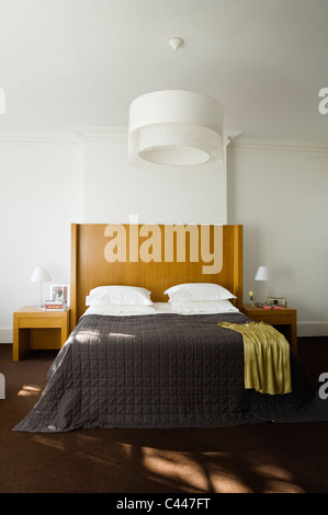 Lit double avec couette et lit en bois blanc dans une chambre avec un grand ombrage léger Banque D'Images