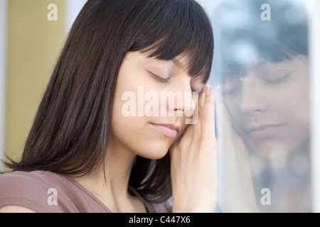 Une femme avec les yeux fermés appuyé contre une fenêtre Banque D'Images