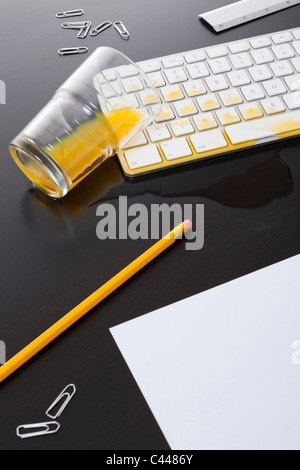 Un verre de jus d'orange renversé sur le clavier d'un ordinateur Banque D'Images