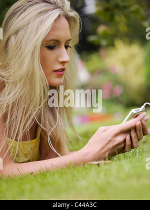 Une femme allongée dans l'herbe de l'écoute d'un MP3 player Banque D'Images