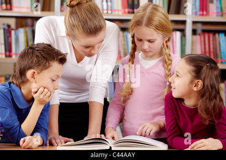 Portrait des élèves et l'enseignant lire et discuter livre intéressant dans la bibliothèque Banque D'Images