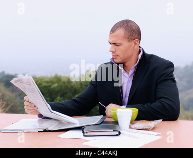 Un homme lit un journal et prendre le petit déjeuner dehors Banque D'Images