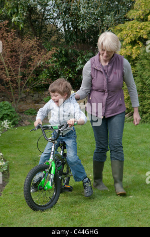 L'enseignement de la grand-mère petit-fils à faire du vélo dans un jardin arrière Banque D'Images