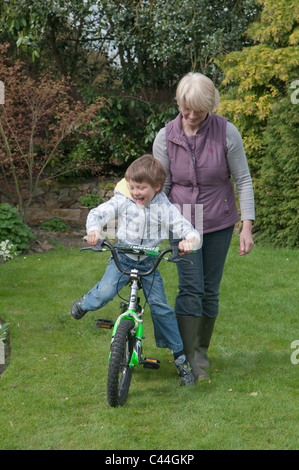 L'enseignement de la grand-mère petit-fils à faire du vélo dans un jardin arrière Banque D'Images