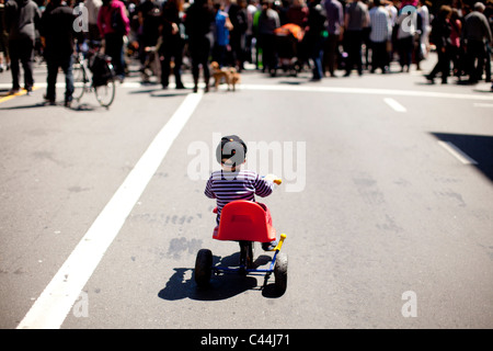 Enfant monte un tricycle sur une route derrière les gens à San Francisco, Californie pendant un mois à la clôture de la rue. Banque D'Images