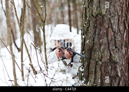 Soldat dans le but de camouflage blanc avec fusil de sniper en forêt d'hiver. Banque D'Images