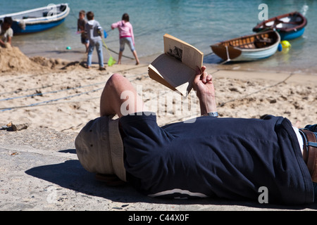 L'homme de lire un livre dans le soleil à la plage en Angleterre Banque D'Images