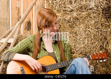 Pays jeune red-hair woman playing guitar in barn Banque D'Images