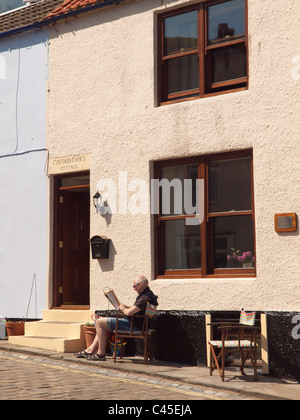 Un homme assis à l'extérieur de Captain Cook's Cottage à Staithes North Yorkshire maintenant une maison privée Banque D'Images