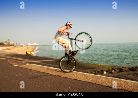 Jeune homme faisant wheelie astuces sur son vélo BMX stunts Banque D'Images