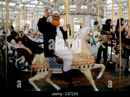 Homme avec barbe rouge en habit religieux vagues et sourit à caméra sur merry go round à San Francisco Banque D'Images