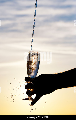 L'eau est versée dans une flûte à champagne. Silhouette Banque D'Images