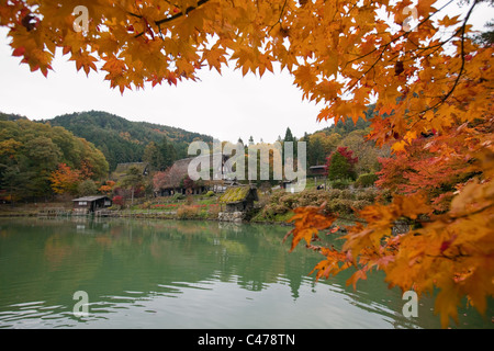 Les feuilles d'automne, au toit de chaume traditionnel restauré des maisons, et l'étang à Hida-no-Sato Folk Village, Takayama, Gifu, Japon. Banque D'Images