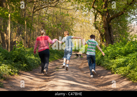 Une mère et ses deux fils n 1 , 2 , 3 , saut en marchant le chien sur une voie de pays au printemps au Royaume-Uni Banque D'Images