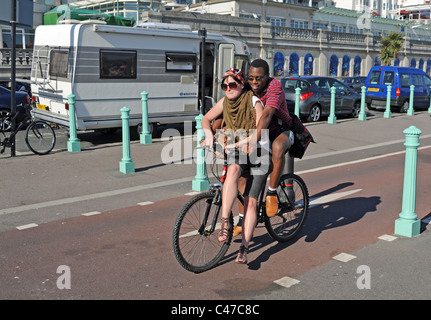 Couple Profitez d'une balade en vélo le long de front de mer de Brighton avec femme en équilibre sur le vélo cross bar UK Banque D'Images