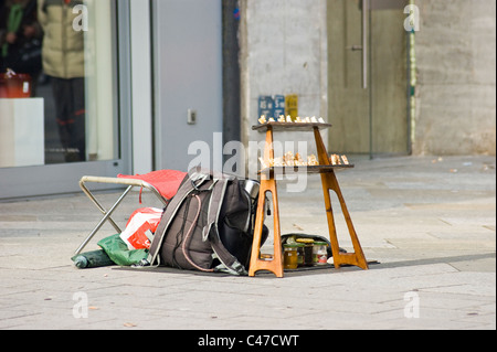 Configuration de rue avec un sac à dos, un tabouret pliant et un petit écran d'échecs disposés sur un trottoir dans une zone commerciale urbaine. Banque D'Images