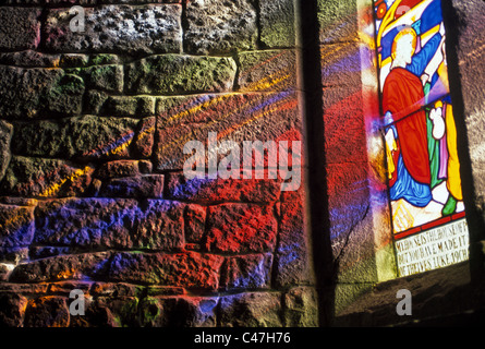La lumière du soleil réfractée à travers un vitrail à motifs colorés jette sur le mur de pierre d'une vieille église en Adare, Irlande. Banque D'Images