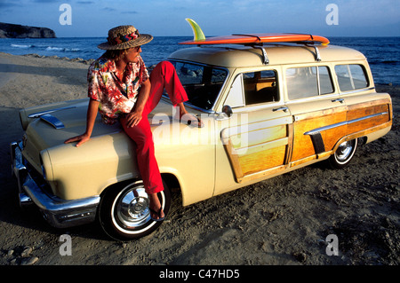 Un surfeur de la Californie se détend sur son classique 1952 Mercure woodie station wagon alors que le soleil se couche sur l'océan Pacifique à Laguna Beach en Californie, USA. Banque D'Images