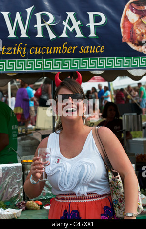 Une femme à l 'vintage' Virginia Wine Festival posant avec un verre de vin et des cornes du diable, en face d'un stand de vendeurs d'aliments. Banque D'Images