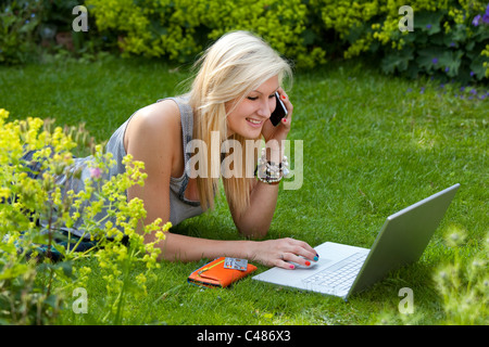 Jeune fille sur moblie phone alors que sur internet, à discuter et à socialiser sur ordinateur portable sans fil dans le jardin Banque D'Images