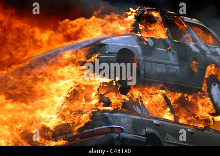 Les voitures sur le feu à un brasier dans un parc à ferrailles Banque D'Images