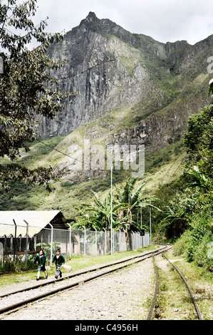 Deux enfants de l'école en uniformes verts à pied le long de la voie ferrée qui partent de l'usine hydroélectrique à Aguas Calientes, Pérou Banque D'Images