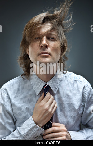 Portrait de l'homme à sur l'oxford shirt ajuste sa cravate alors que ses cheveux bruns autour de coups. Banque D'Images