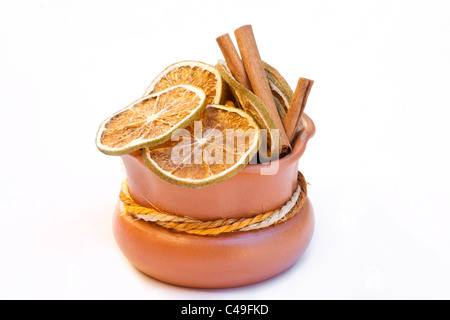 Tranches d'orange séchée et des bâtons de cannelle dans un pot en terre cuite sur fond blanc Banque D'Images